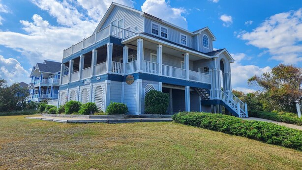 A large, two-story house with a balcony and a porch, surrounded by a well-maintained lawn.