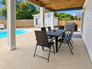 An outdoor patio with a pool, a covered seating area, and a wooden fence.
