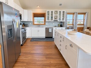 A modern kitchen with white cabinetry, a stainless steel refrigerator, a built-in oven, and a large island with a bowl.