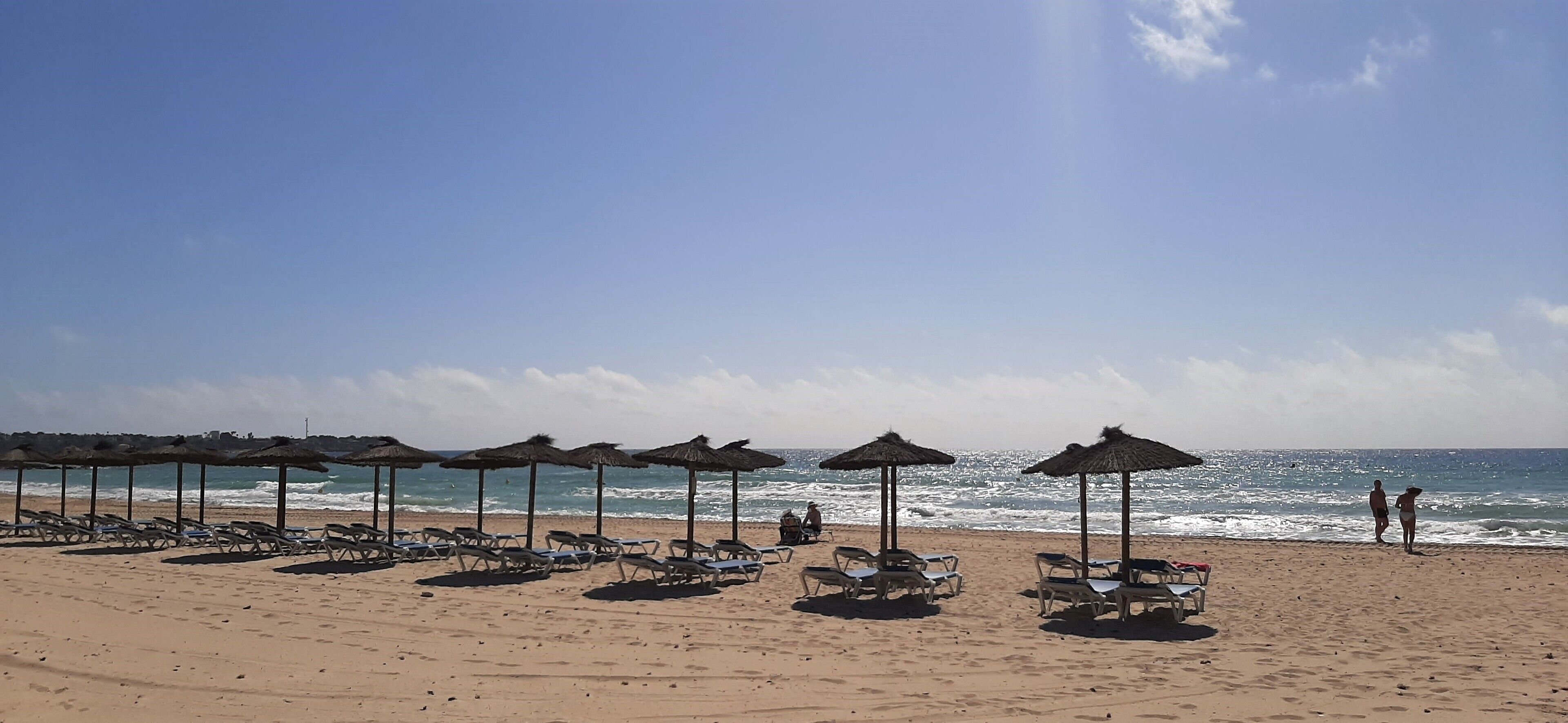 Een strand met rijen ligbedden en parasols, een heldere lucht en de oceaan op de achtergrond.