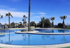 Una piscina amplia y cristalina con palmeras y cielo despejado.
