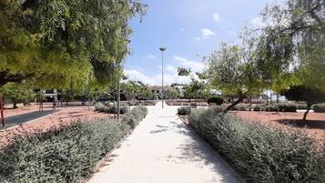 A pathway flanked by neatly trimmed hedges and trees, leading towards a building with a red-tiled roof.