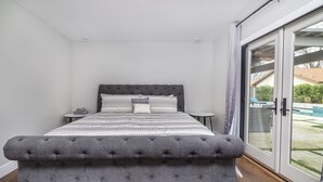 A bedroom with a large bed, a bedside table, and a sliding glass door leading to an outdoor area. - Comfy House W/ Big Pool (Elk Grove)
