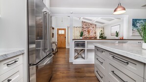 A modern kitchen with stainless steel appliances, white cabinetry, and a wooden floor. - Comfy House W/ Big Pool (Elk Grove)