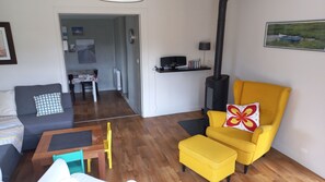 Una sala de estar con sofá, un sillón amarillo, una mesita y una chimenea.