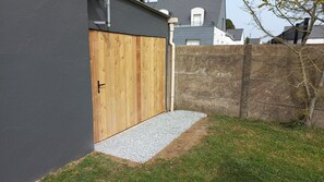 Una puerta de madera con manija metálica, pared de concreto y un sendero de grava que conduce a una zona con césped.