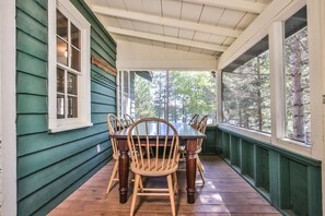Un portico coperto con un tavolo e sedie in legno, rivestimento verde e ampie finestre.
