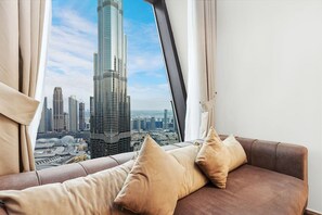 A room with a view of a tall skyscraper, a brown sofa with cushions, and a window with curtains.