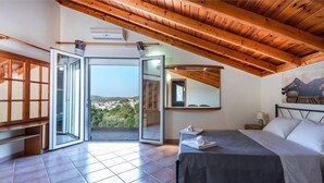 A bedroom with a bed, a nightstand, a mirror, and a view of the outdoors. - villa aphrodite (Maritsa)
