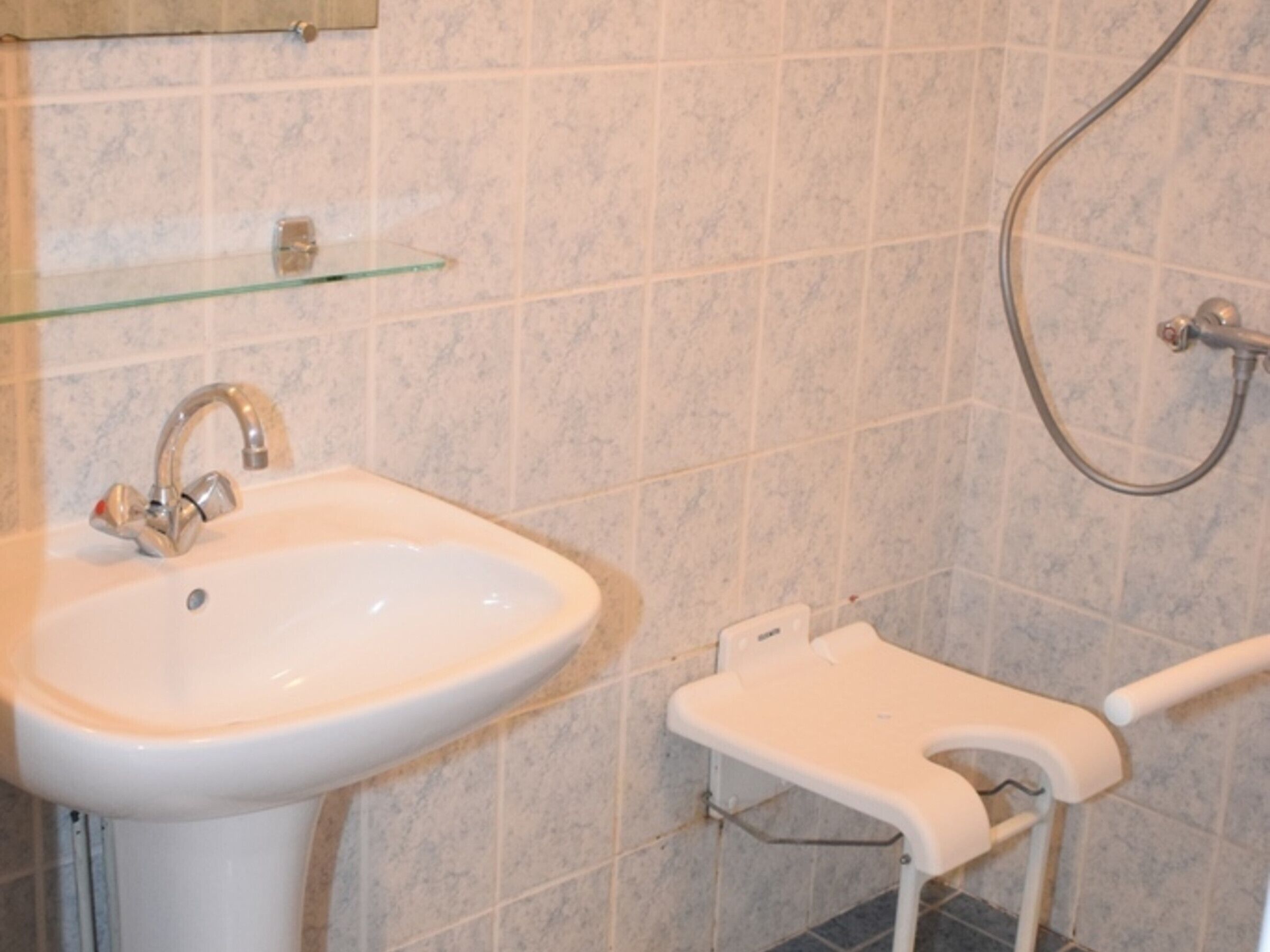 Un baño con lavamanos blanco, repisa de vidrio y zona de ducha.