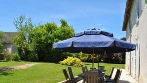 An outdoor patio with a table and chairs under a large umbrella, surrounded by greenery and a building. - Spacious Historic Presbytery, Sleeps 15, Garden, WiFi, Near Châteaux & La Roche-Posay (Bossay-sur-Claise)