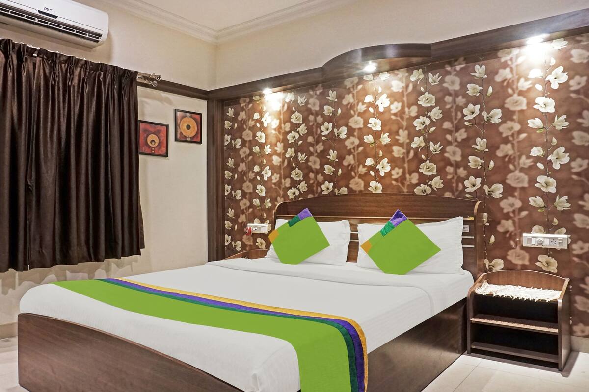 A hotel room with a bed, a nightstand, an air conditioner, and floral wallpaper.