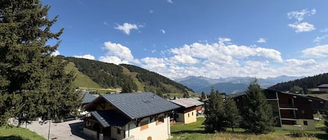 Un chalet de montagne avec un toit en pente, entouré de verdure et offrant une vue sur les montagnes lointaines.