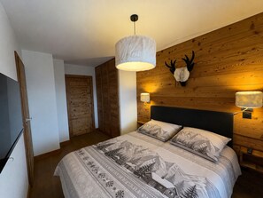 A bedroom with a large bed, wooden walls, a mounted deer head, and a hanging light fixture. - New 4-Room Apt 8 Guests, Pets Allowed, Parking (Hauteluce)