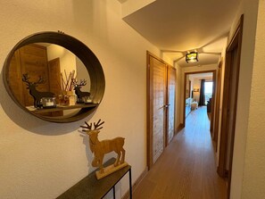 Un pasillo con piso de madera, un espejo redondo en la pared y un pequeño estante de madera con una figura de venado.