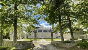 A courtyard with a stone pathway leading to a large building with multiple windows and a central entrance. - 17th century château in its original state, near Bayeux and the D-Day landing beaches (Vaux-sur-Seulles)