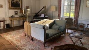 A living room with a grand piano, a sofa, a chair, and a table with a lamp. - 17th century château in its original state, near Bayeux and the D-Day landing beaches (Vaux-sur-Seulles)