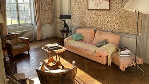 A room with a floral wallpaper, a sofa, a chair, a table with books, and a lamp. - 17th century château in its original state, near Bayeux and the D-Day landing beaches (Vaux-sur-Seulles)