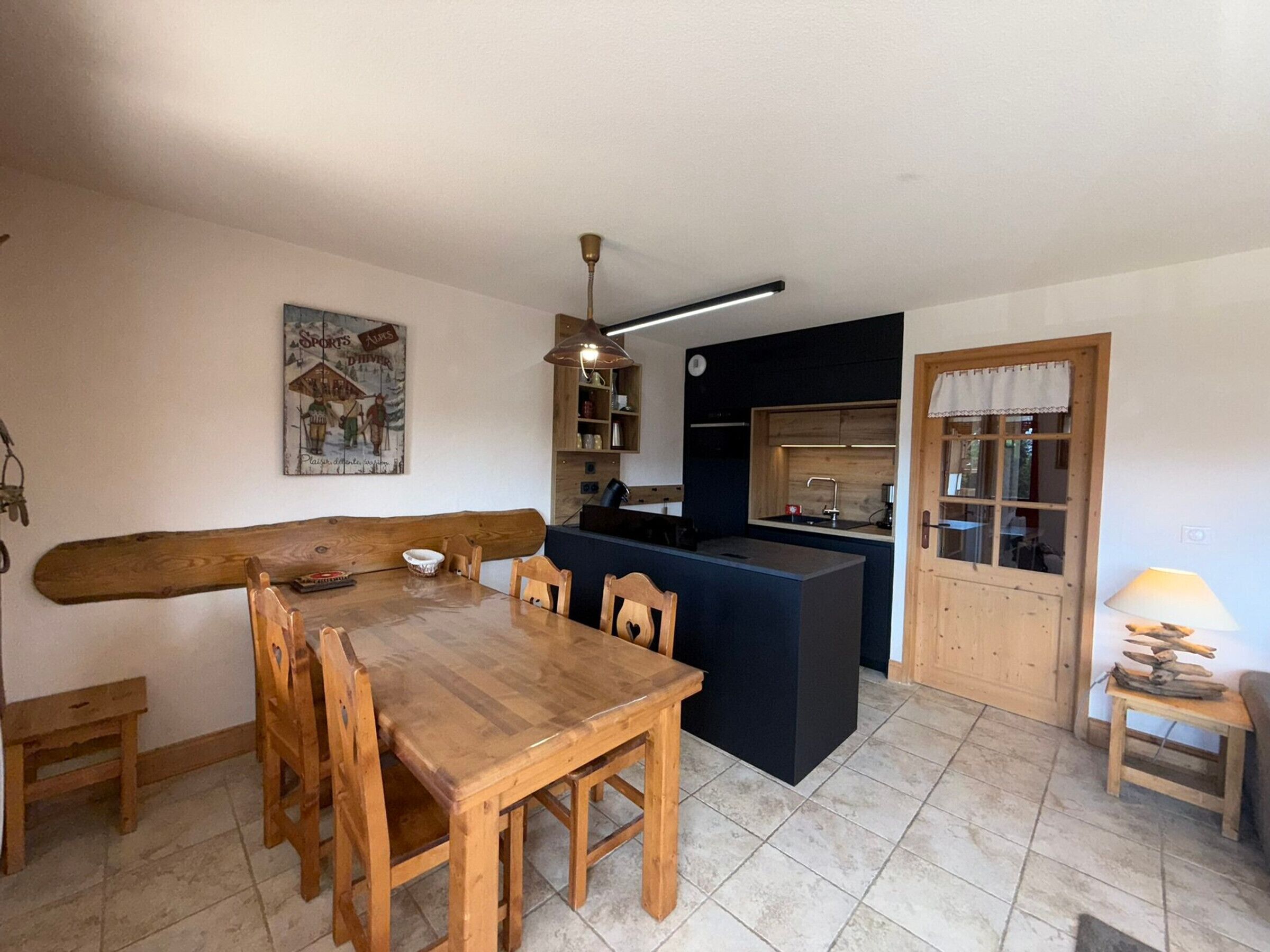 A dining area with a wooden table and chairs, a kitchen with a black countertop, and a wooden door.