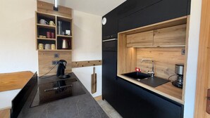 Une cuisine compacte dotée d’un plan de travail noir, de meubles en bois, d’un évier encastré et d’une machine à café.