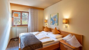 A bedroom with a bed, bedside tables, a radiator, a window with curtains, and wall-mounted lamps. - Holiday Apartment "Alpenhof Lodge Ifinger" with Mountain View, Breakfast, Wellness & Wi-Fi (Saltaus)