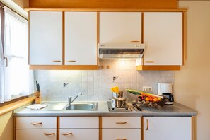 A kitchen with white cabinets, a stainless steel sink, a coffee maker, and a fruit basket on the counter.