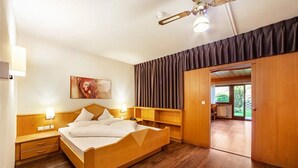 A hotel room with a wooden bed, bedside tables, a ceiling fan, a painting, and a view of the outdoors.