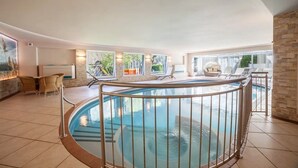A pool area with a curved design, sun loungers, and a view of a playground through large windows.