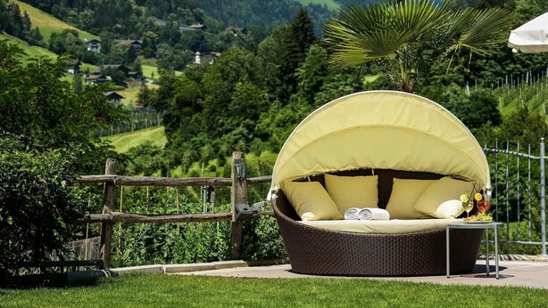 A wicker outdoor seating area with a canopy, surrounded by a wooden fence and lush greenery.