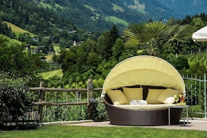 Un espace de détente extérieur aménagé avec des meubles en osier, doté d’un auvent et entouré d’une clôture en bois et d’une végétation luxuriante.