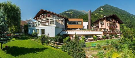 A hotel with multiple floors, outdoor seating, and a mountainous backdrop.