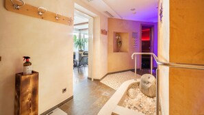 A hallway with a wooden coat rack, a stone-tiled floor, a small stone fountain, and a door leading to another room.