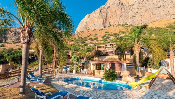 Un espace piscine avec des chaises longues, un toboggan et une vue sur les montagnes en arrière-plan.