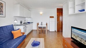 Un espacio habitable compacto con sofá, mesa de comedor, televisor y kitchenette.