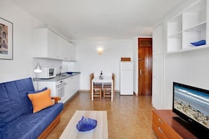 Un espacio habitable compacto con sofá, mesa de comedor, televisor y kitchenette.