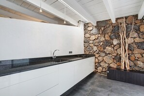 A modern kitchen with a stone wall, a black countertop, and a built-in stove. - 'La Bodeguita House' with Sea Views, Private Terrace and Wi-Fi (Haría)