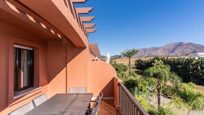 A balcony with a wooden table and chairs, a window with curtains, and a view of mountains and greenery. - Apartment 'Duplex Estepona' with Mountain View, Wi-Fi and Air Conditioning (Estepona)
