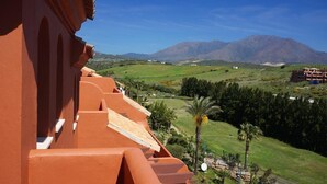 A view of a building with a red facade and a balcony overlooking a green landscape with mountains in the background. - Apartment 'Duplex Estepona' with Mountain View, Wi-Fi and Air Conditioning (Estepona)