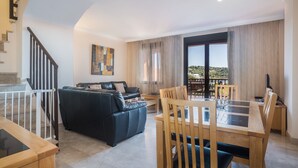 A modern living room with a sofa, dining table, and chairs, a staircase, and a large window with a view. - Apartment 'Duplex Estepona' with Mountain View, Wi-Fi and Air Conditioning (Estepona)