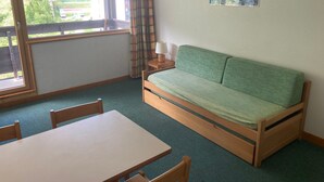 A room with a green sofa, a wooden table, and a window with curtains.