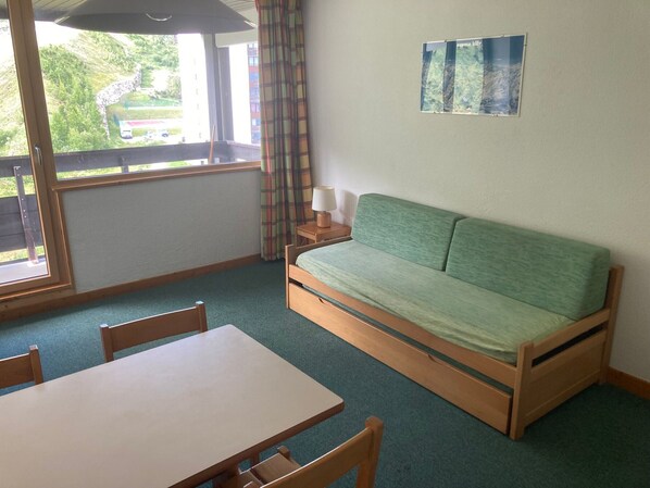 Ein Zimmer mit einem grünen Sofa, einem Holztisch und einem Fenster mit Vorhängen.