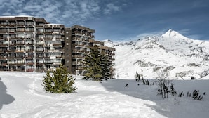 A multi-story building with balconies, a snow-covered mountain in the background, and a clear sky.