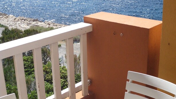 A balcony with a white chair and a table, overlooking a rocky coastline and the sea. - Ile du Frioul, 4-bed apartment at the foot of the calanques (Marseille)