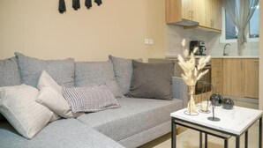 A modern living room with a grey sofa, a small coffee table, and a kitchen area with wooden cabinets and a window. - Deatached apartment with shared pool in Tersanas Chania 2 minutes from the beach (chania)