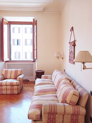 A living room with a sofa, armchair, and a window with open shutters. - Roman Holidays Boutique (Rome)