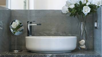 Un baño con lavamanos blanco, un espejo y un florero con flores blancas.