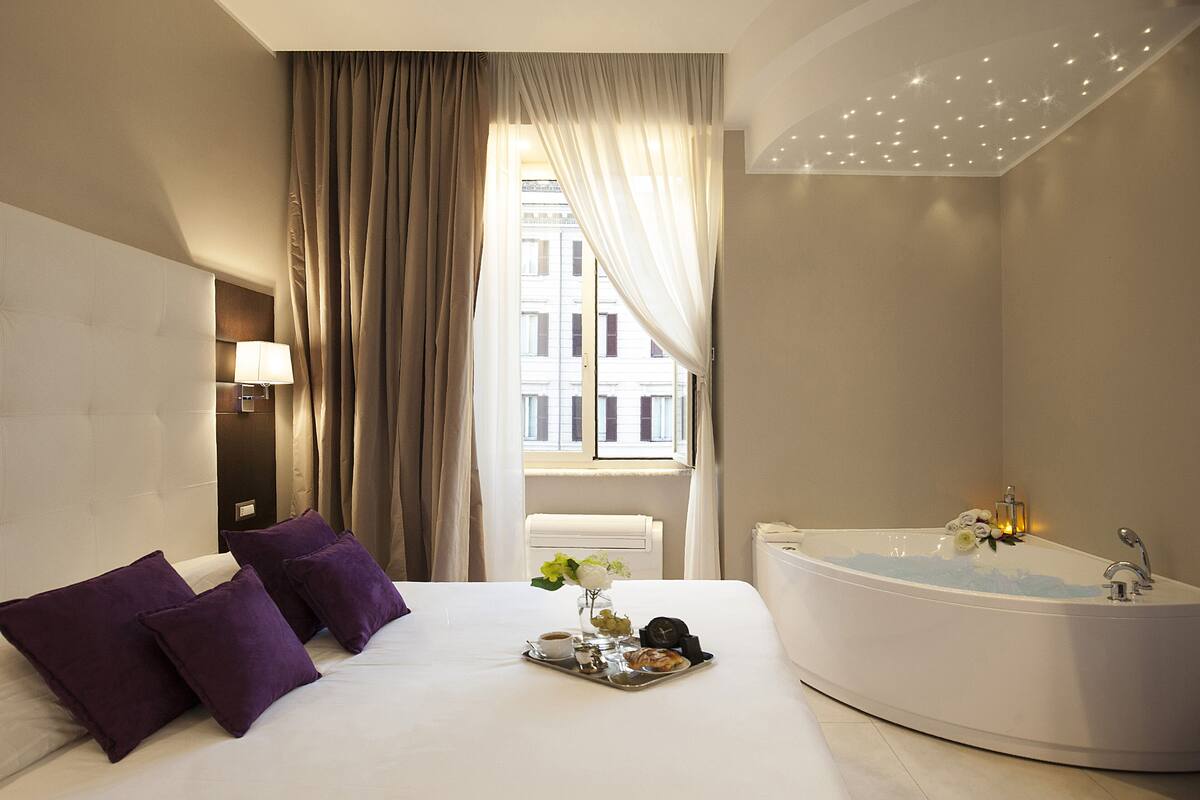 A hotel room with a large bed, a bathtub, and a window with curtains.