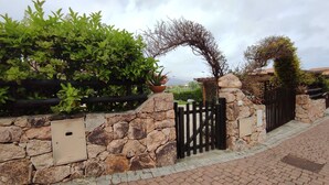 A stone wall with a metal gate, lush greenery, and a potted plant. - Villa Janas with private pool🏖️ (Budoni sardegna)