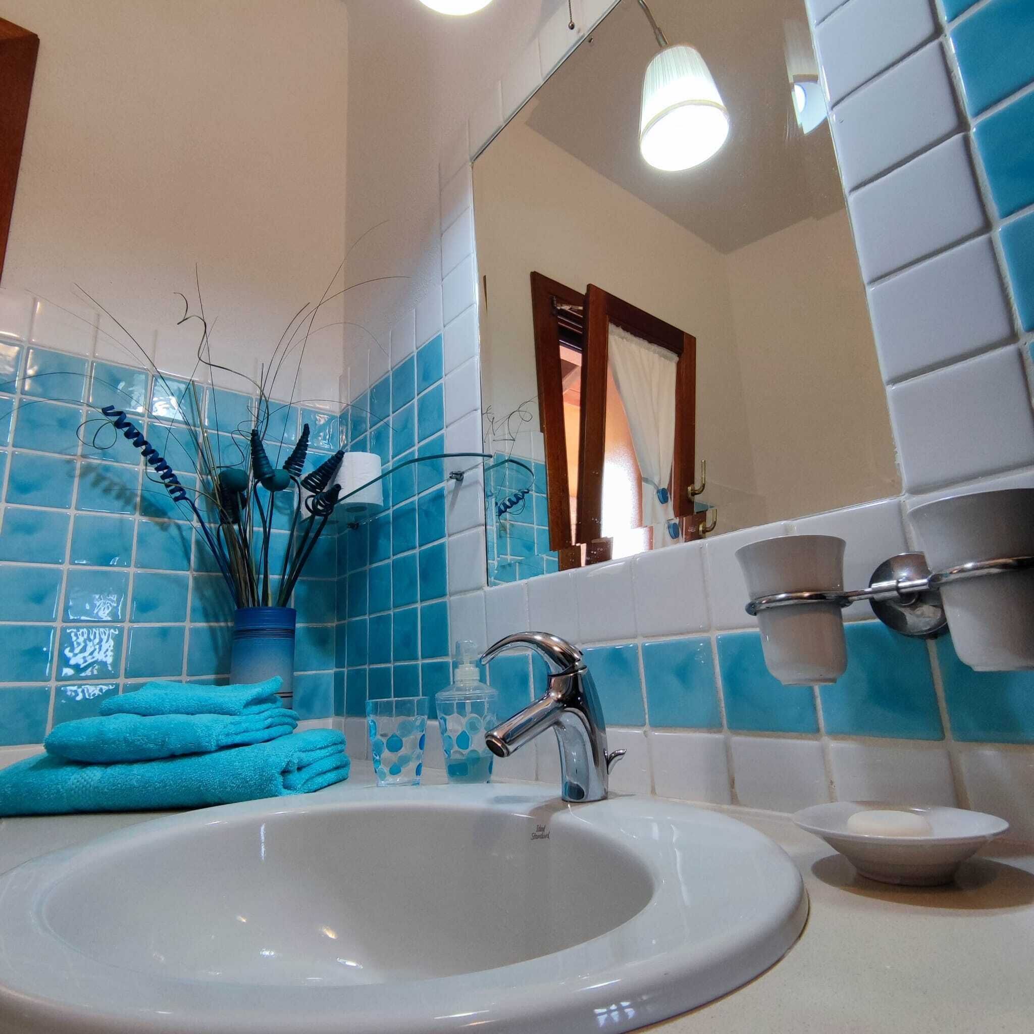 A bathroom with a white sink, blue tiles, a mirror, and a towel rack.