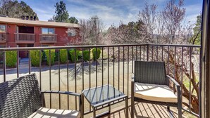 Un balcon avec deux fauteuils en osier et une petite table, donnant sur une rue et un immeuble doté d’un balcon.